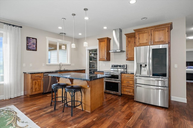 kitchen with stainless steel appliances, brown cabinetry, a sink, wall chimney range hood, and a kitchen island