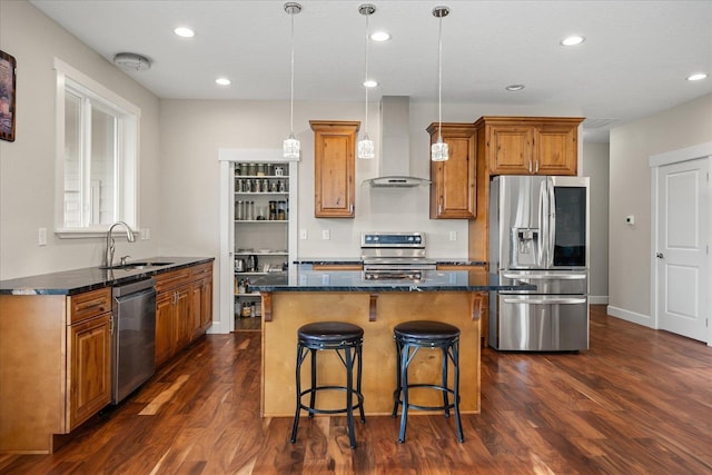 kitchen featuring dark wood-style flooring, brown cabinets, appliances with stainless steel finishes, a sink, and wall chimney range hood