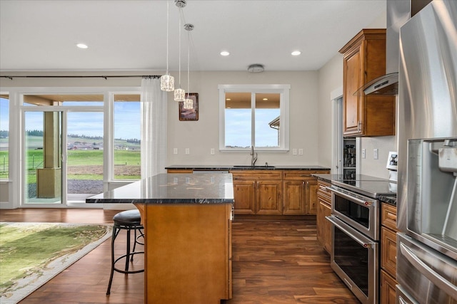 kitchen featuring brown cabinets, wall chimney exhaust hood, stainless steel appliances, and a sink