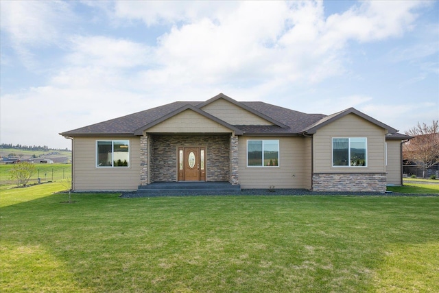 view of front of home with stone siding, a front lawn, and roof with shingles