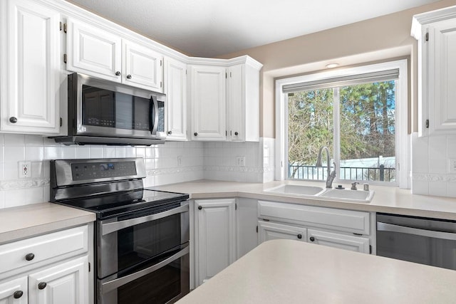 kitchen with stainless steel appliances, a sink, white cabinets, light countertops, and decorative backsplash