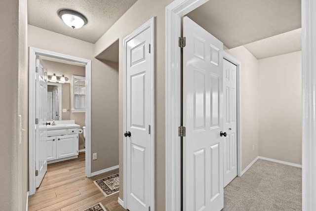 corridor featuring baseboards, a sink, a textured ceiling, and light wood finished floors