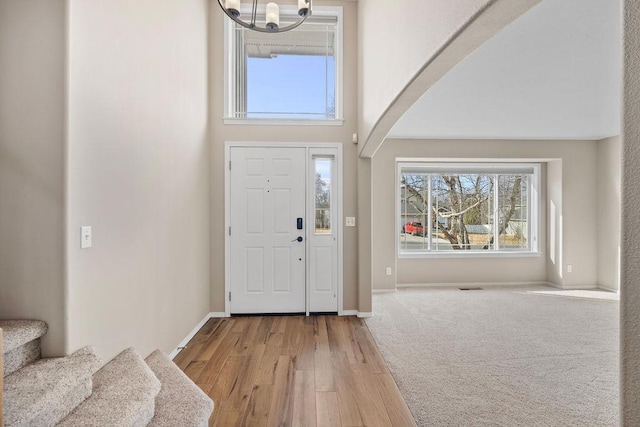 entrance foyer featuring arched walkways, wood finished floors, a towering ceiling, baseboards, and stairs