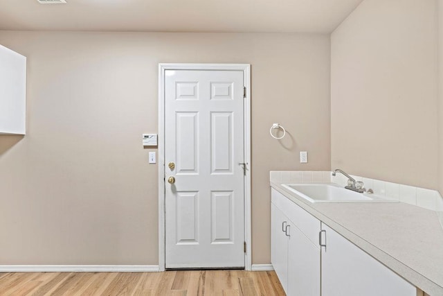 clothes washing area with light wood finished floors, a sink, visible vents, and baseboards