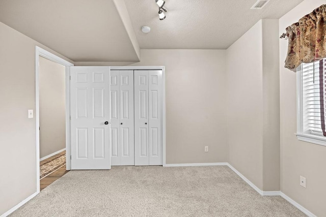 unfurnished bedroom featuring baseboards, visible vents, a textured ceiling, carpet floors, and a closet