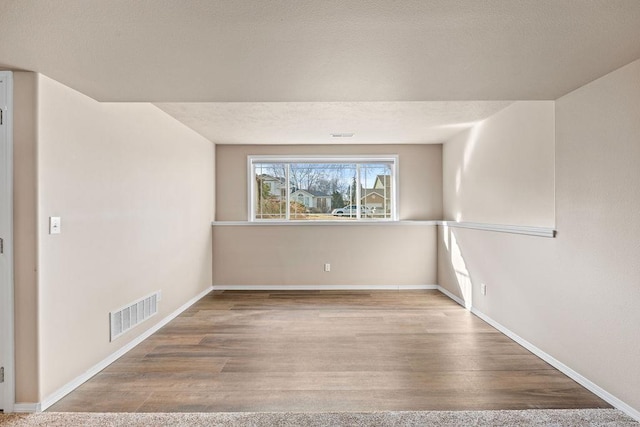 unfurnished room featuring a textured ceiling, wood finished floors, visible vents, and baseboards