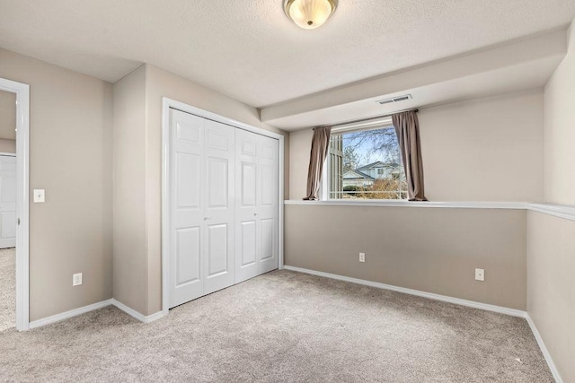 unfurnished bedroom featuring carpet, a textured ceiling, visible vents, and a closet