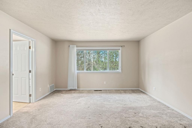 spare room with carpet floors, baseboards, visible vents, and a textured ceiling