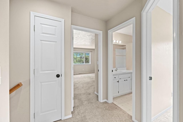 corridor featuring baseboards, a sink, and light colored carpet