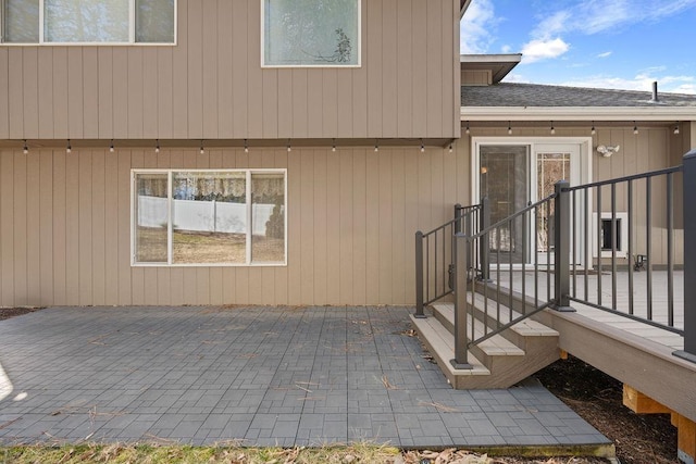 entrance to property with roof with shingles and a patio area