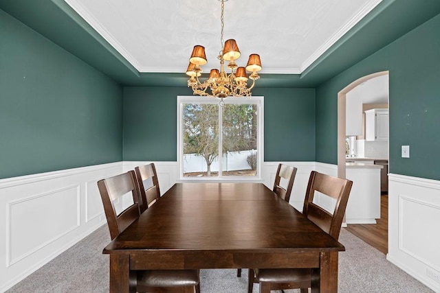 dining space featuring arched walkways, wainscoting, a raised ceiling, and an inviting chandelier