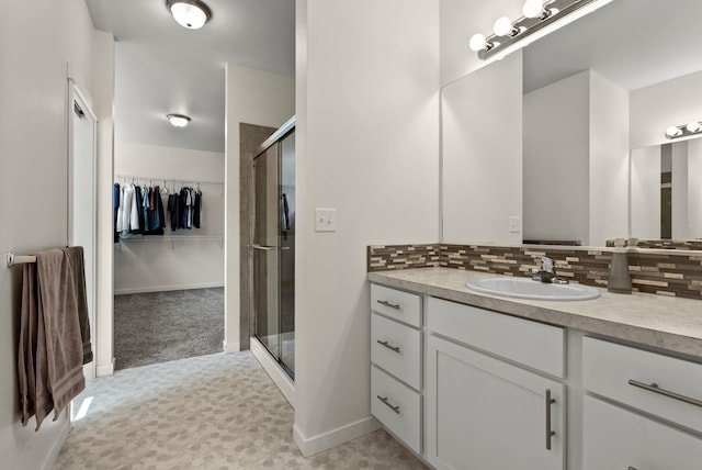 bathroom featuring a walk in closet, decorative backsplash, a shower stall, vanity, and baseboards