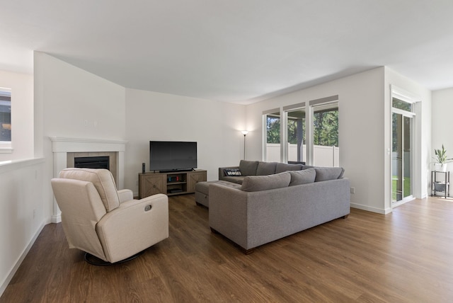 living room featuring dark wood-style flooring, a tiled fireplace, and baseboards