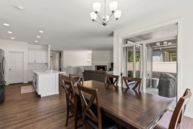 dining area featuring a lit fireplace, recessed lighting, dark wood finished floors, and an inviting chandelier