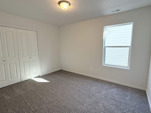 unfurnished bedroom featuring a textured ceiling, carpet floors, visible vents, baseboards, and a closet