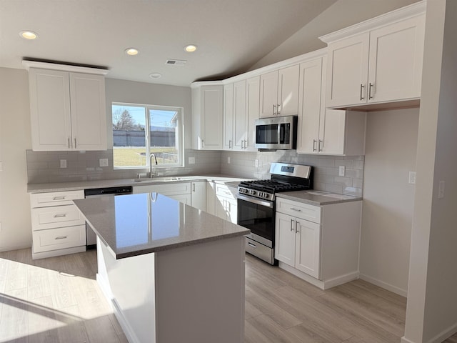 kitchen with stainless steel appliances, a sink, white cabinetry, visible vents, and a center island