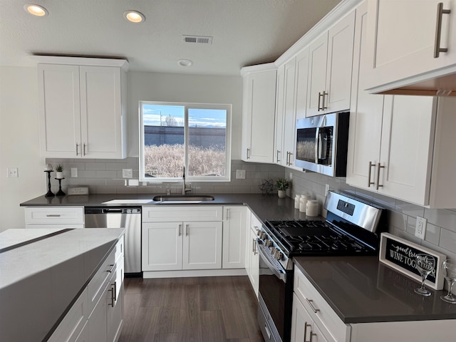 kitchen featuring stainless steel appliances, dark countertops, visible vents, and a sink