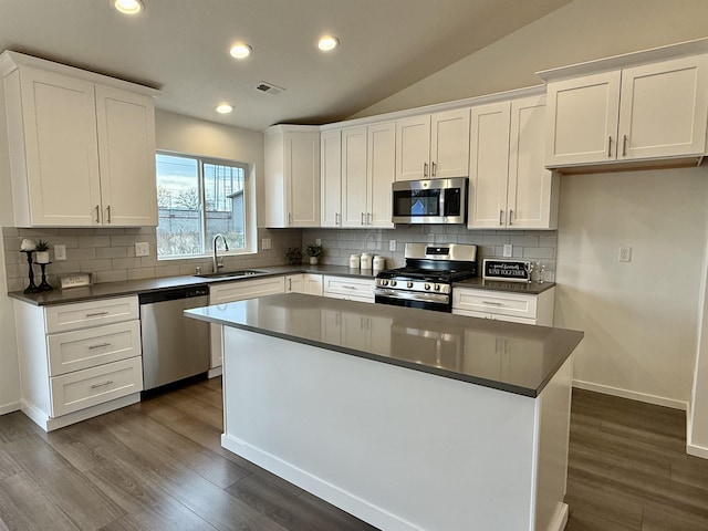 kitchen featuring dark countertops, visible vents, appliances with stainless steel finishes, vaulted ceiling, and a sink