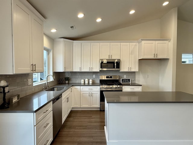 kitchen with dark countertops, appliances with stainless steel finishes, a sink, and lofted ceiling