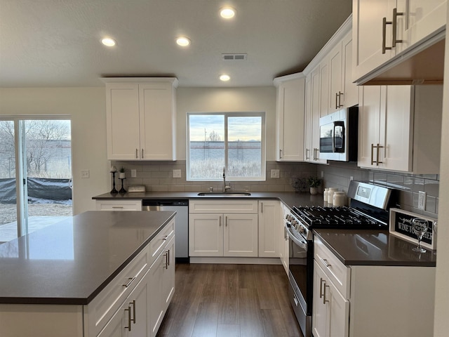 kitchen with appliances with stainless steel finishes, dark countertops, a sink, and visible vents