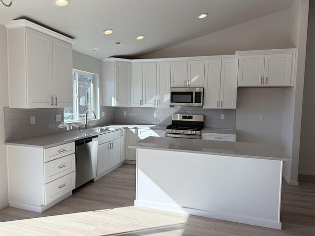 kitchen with lofted ceiling, a kitchen island, stainless steel appliances, white cabinetry, and a sink