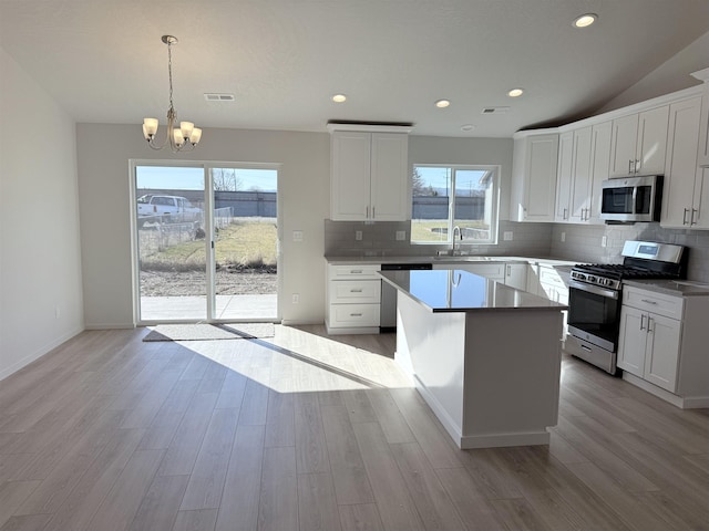 kitchen featuring tasteful backsplash, appliances with stainless steel finishes, a center island, light wood-type flooring, and a sink