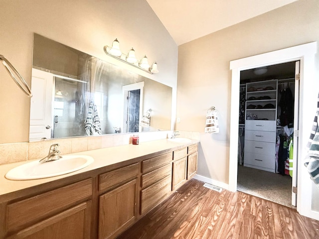 bathroom featuring a stall shower, a sink, a spacious closet, and wood finished floors