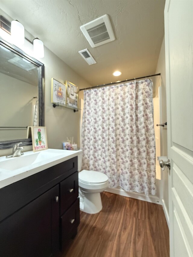 full bathroom featuring toilet, vanity, wood finished floors, and visible vents