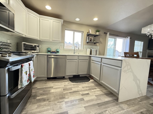 kitchen with a toaster, a peninsula, stainless steel appliances, a healthy amount of sunlight, and a sink