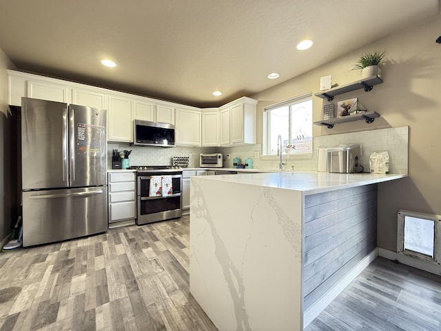 kitchen with a peninsula, appliances with stainless steel finishes, decorative backsplash, and white cabinets