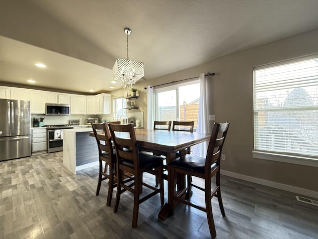 dining space featuring a notable chandelier, visible vents, baseboards, and wood finished floors