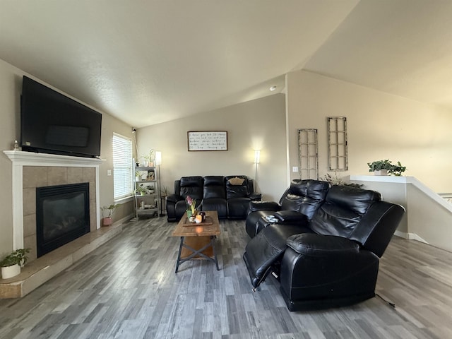 living room with lofted ceiling, baseboards, a tiled fireplace, and wood finished floors