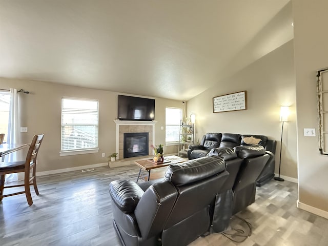 living room featuring vaulted ceiling, wood finished floors, a tile fireplace, and baseboards