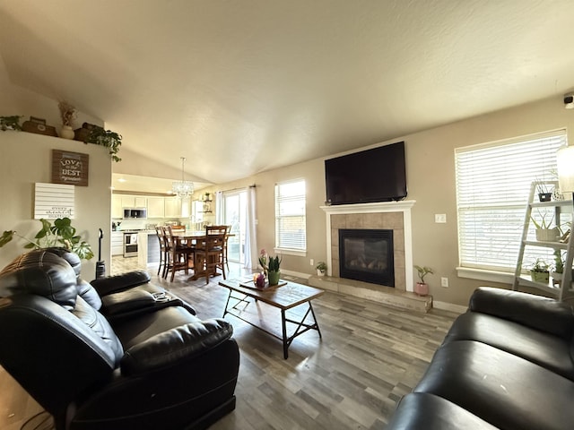 living room with a tile fireplace, vaulted ceiling, baseboards, and wood finished floors