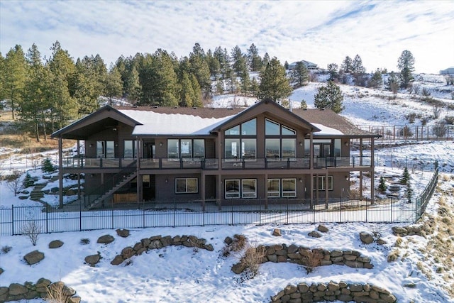 snow covered house with fence private yard, a deck, and stairs