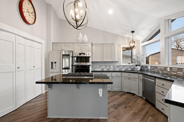 kitchen with lofted ceiling, a sink, an inviting chandelier, stainless steel appliances, and backsplash