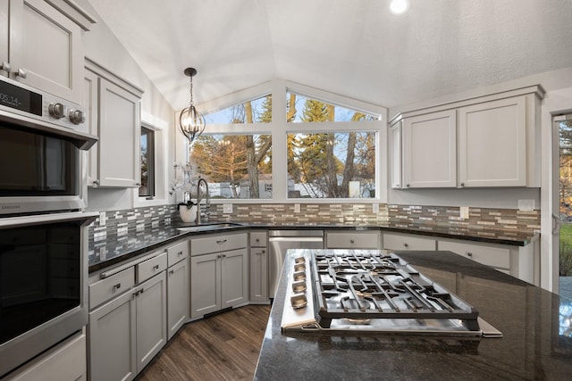 kitchen with dark stone counters, dark wood-style floors, appliances with stainless steel finishes, vaulted ceiling, and a sink