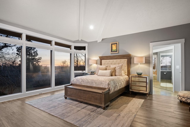 bedroom with vaulted ceiling with beams, a textured ceiling, and wood finished floors