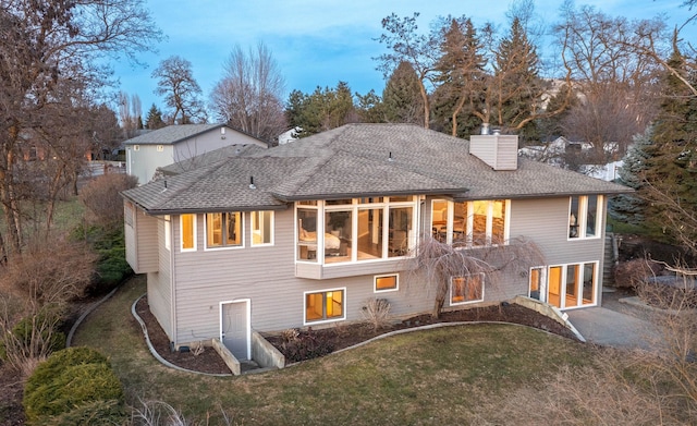 rear view of house featuring driveway, a shingled roof, a chimney, and a yard