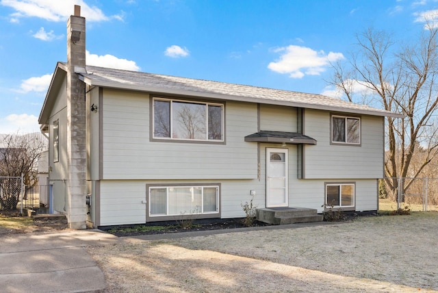 bi-level home with a chimney and fence