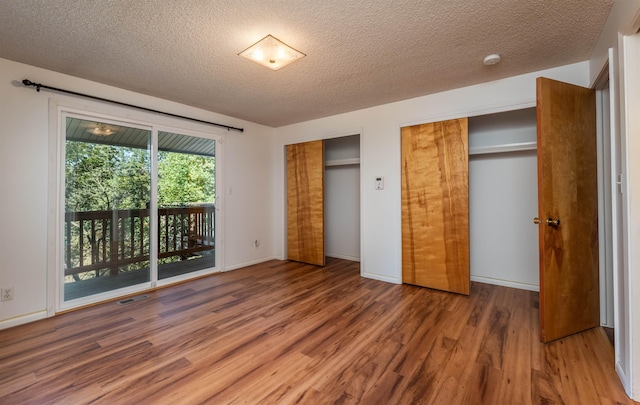 unfurnished bedroom with visible vents, wood finished floors, access to exterior, a textured ceiling, and multiple closets