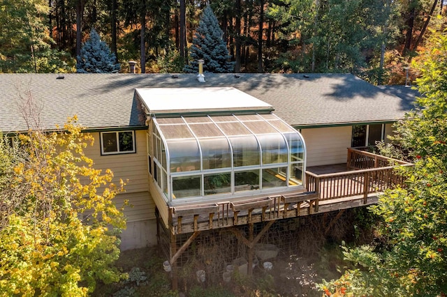 back of house with a shingled roof, a greenhouse, and an outbuilding