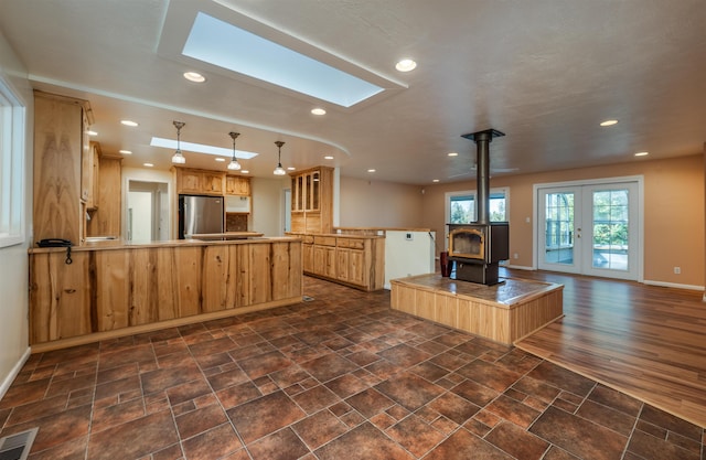 kitchen featuring a skylight, visible vents, freestanding refrigerator, a peninsula, and a wood stove