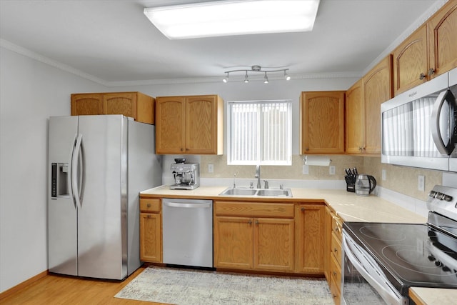 kitchen with crown molding, light countertops, appliances with stainless steel finishes, a sink, and light wood-type flooring