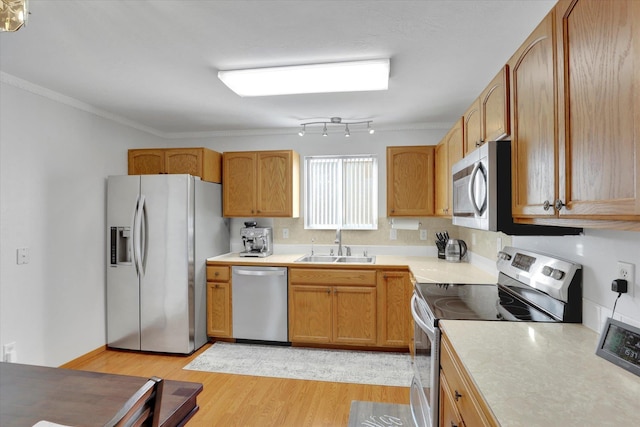 kitchen with light wood finished floors, appliances with stainless steel finishes, light countertops, crown molding, and a sink