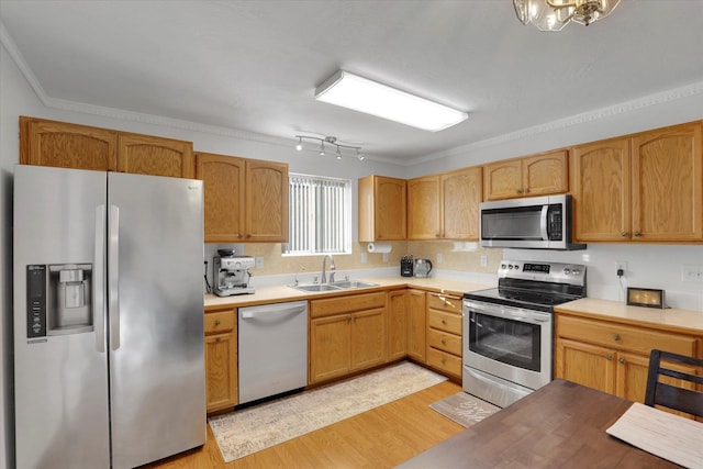 kitchen featuring crown molding, light countertops, light wood-style flooring, appliances with stainless steel finishes, and a sink