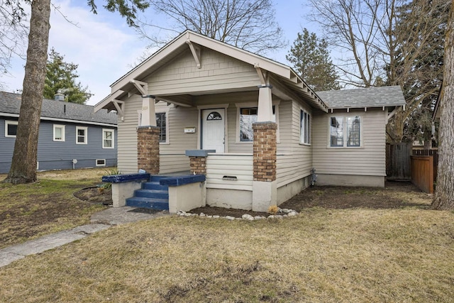 view of front of house with roof with shingles, a front lawn, and fence