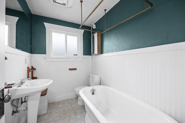 full bathroom with visible vents, toilet, a wainscoted wall, tile patterned flooring, and a freestanding tub