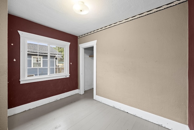 spare room featuring a textured ceiling, wood finished floors, and baseboards