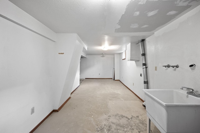 finished below grade area with a textured ceiling, a sink, and baseboards